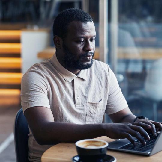 Black Man using Laptop at a Cafe with cup of coffee next to him